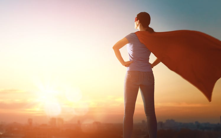 Joyful beautiful young woman in superhero costume posing on sunset background.