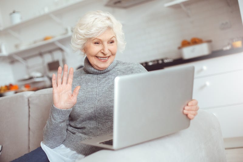 An old woman smiles and waves at her laptop screen
