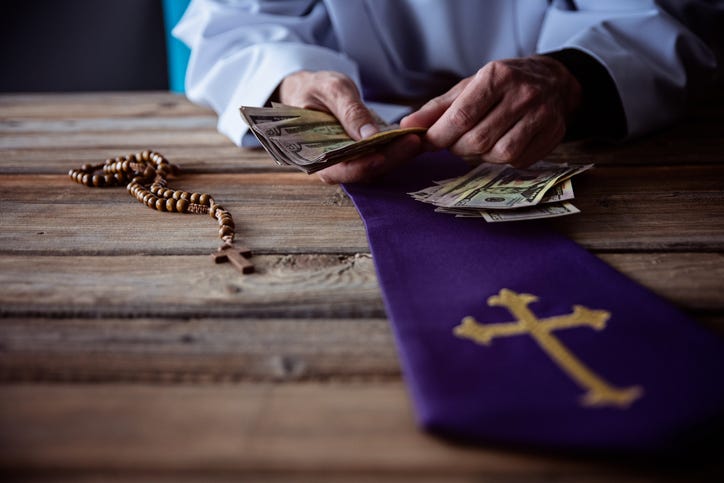 Priest shown counting money on a wooden table. A rosary and mantle are also displayed on the table.