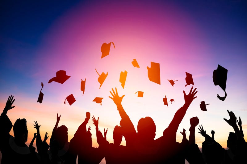 A group of graduates in silhouette toss their caps.