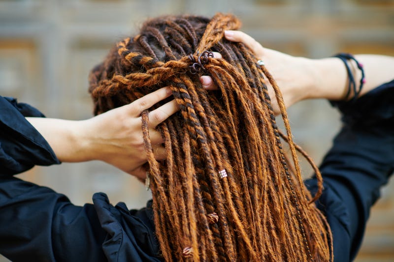 A woman with locs/twists runs her hands through her hair. 