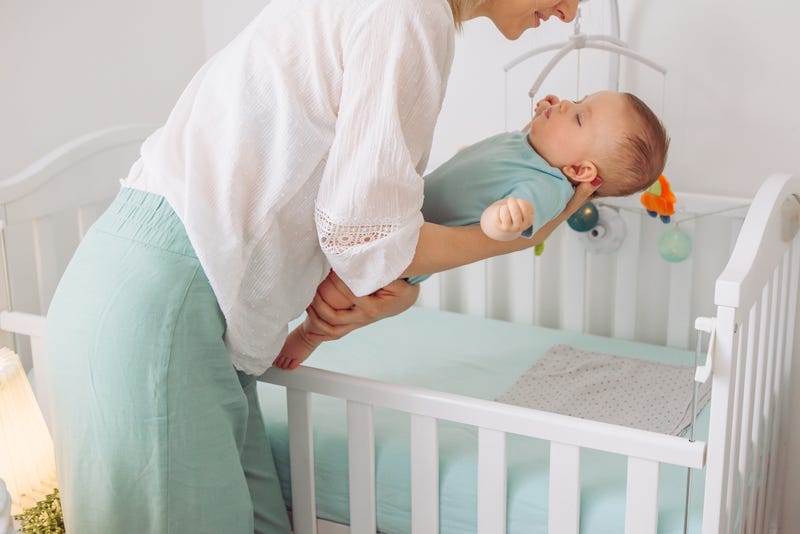 Mother put gently sleeping baby in to the crib