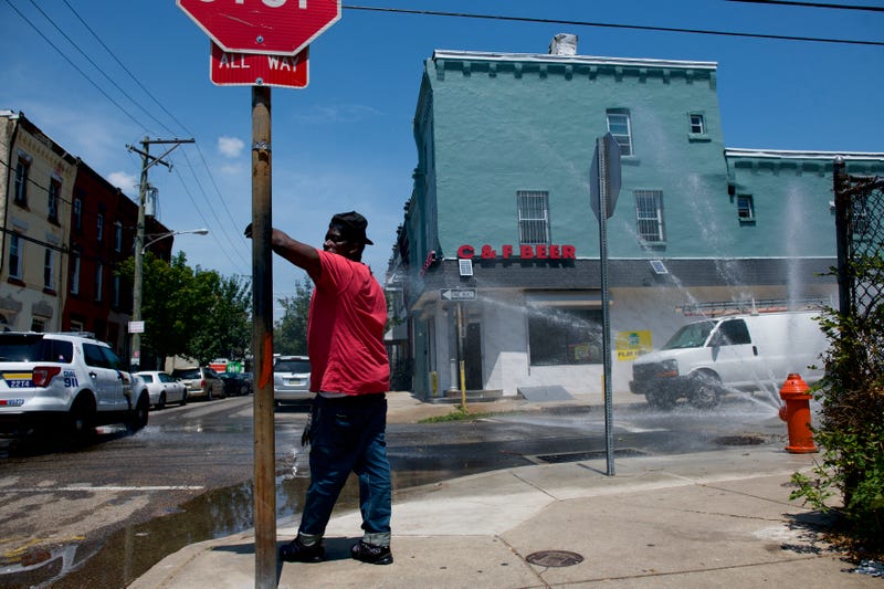 A police car passes, as a man leans on a stop sign beside a spraying fire hydrant in Philadelphia.