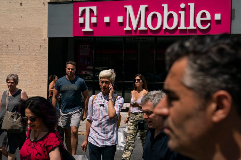 Pedestrians cross an intersection near a T-Mobile store on Sixth Avenue in Manhattan on July 26, 2019 in New York City.