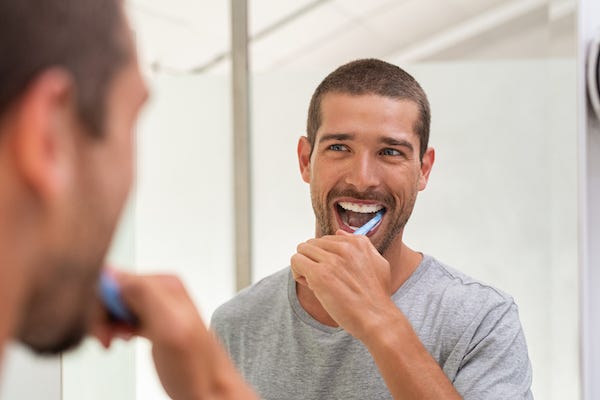 Happy man brushing teeth in the mirror