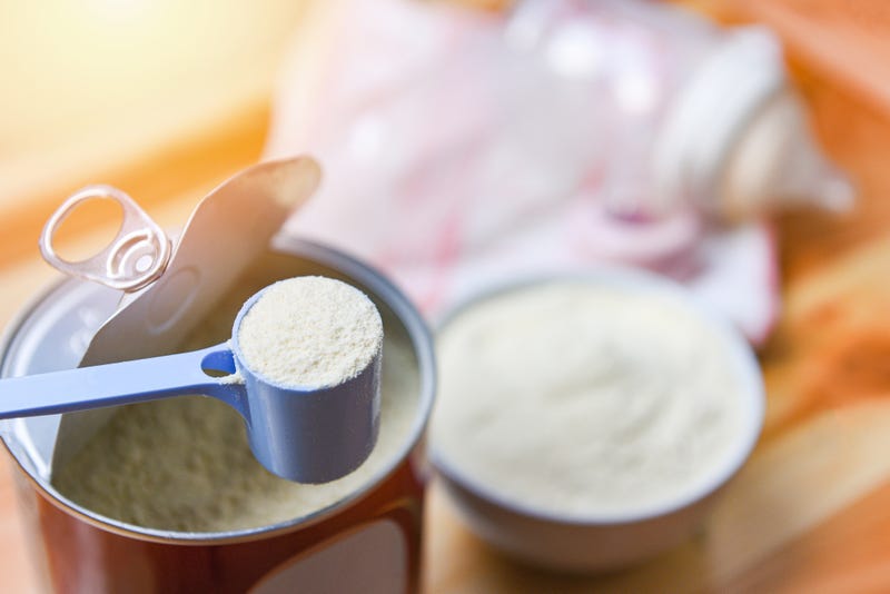 Milk powder in spoon with can and baby bottle milk in bowl on wooden table background