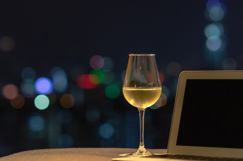A glass with white wine puts on sofa with laptop computer with colorful bokeh light from city.