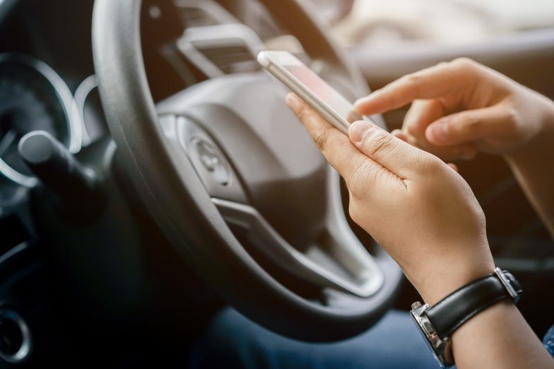 A woman holds a phone while behind the wheel.