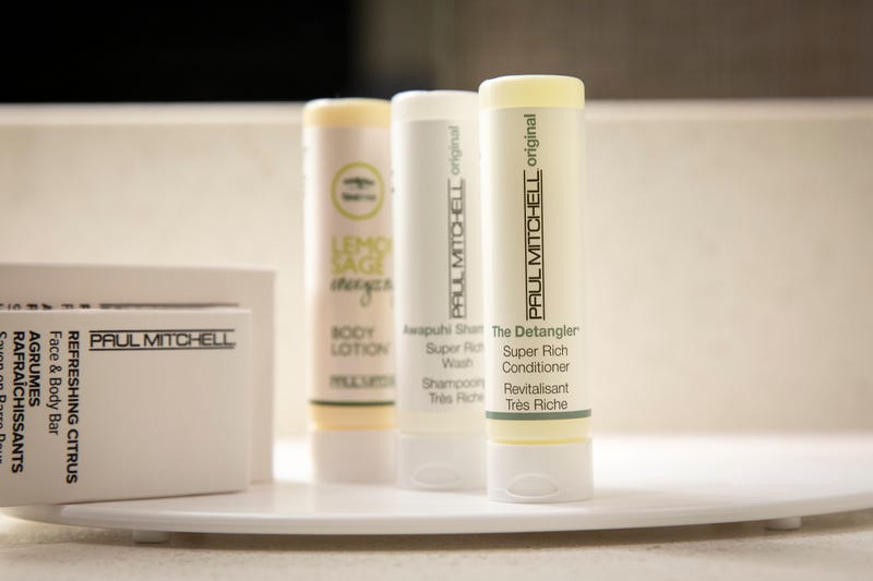 Small plastic bottles of shampoo, conditioner and body lotion sit in a bathroom in a room at a hotel operated by Marriott.