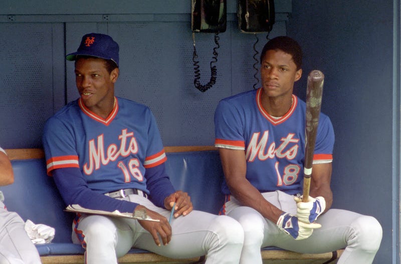 Dwight Gooden #16 and Darryl Strawberry #18 of the New York Mets look on from the dugout during a Major League Baseball game against the Pittsburgh Pirates at Three Rivers Stadium in 1984 in Pittsburgh, Pennsylvania.