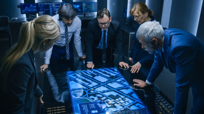High Angle Shot of Team of Government Intelligence Agents Talking while Standing Around Digital Touch Screen Table and Tracking Suspect. Satellite Surveillance Operation in the Monitoring Room.
