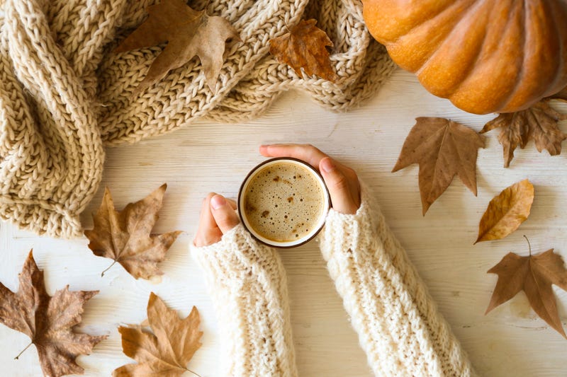 Woman's hands around pumpkin spice late, surrounded by scarf, pumpkin and leaves. 