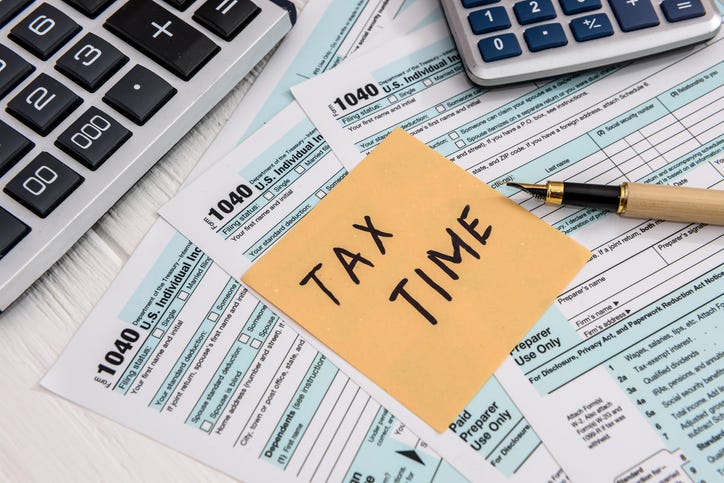 Tax forms, an adding machine and a calculator spread out on a desk. A note stuck to the forms reads "Tax Time."