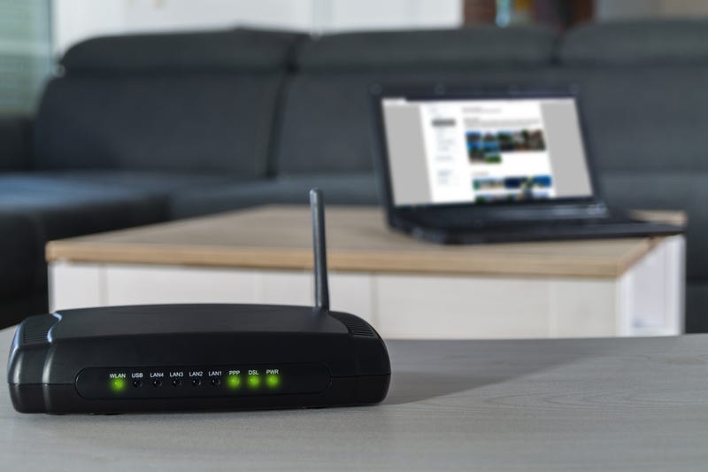 A router on a desk with a laptop in the background.