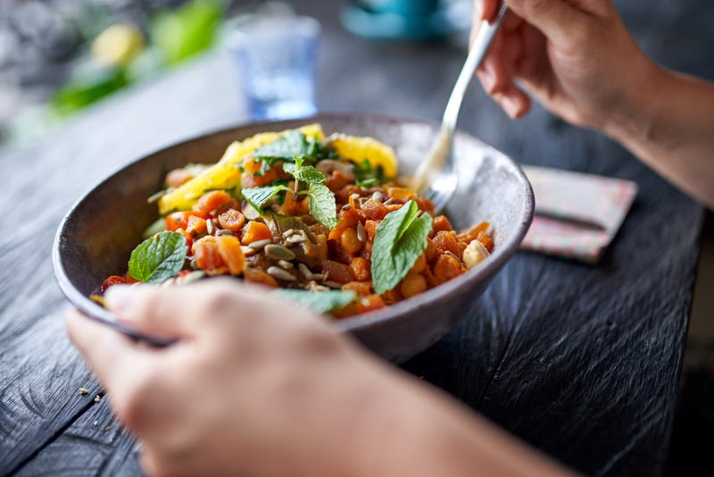 Closeup shot of vegetarian person hands holding gourmet championship game lunch dish with chickpeas mint, fresh herbs and fruit at wooden table.