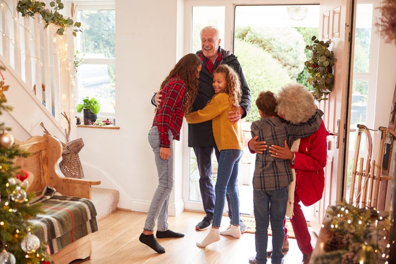 An older couple greet three children in a house decorated for Christmas