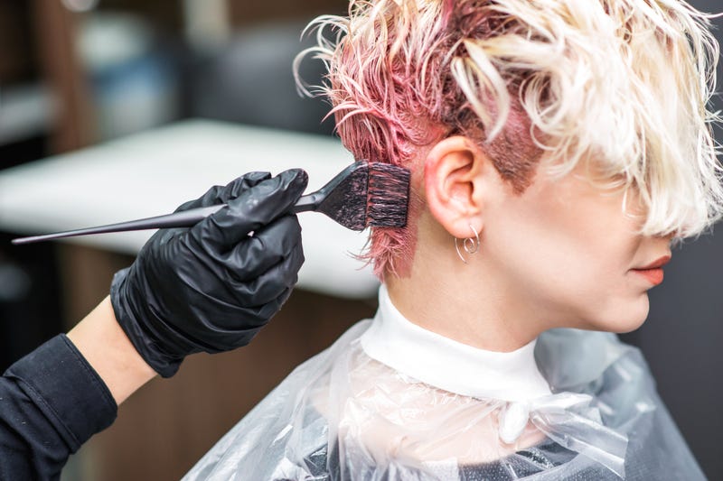 Hairdresser hand in black gloves paints the woman's hair in a pink color