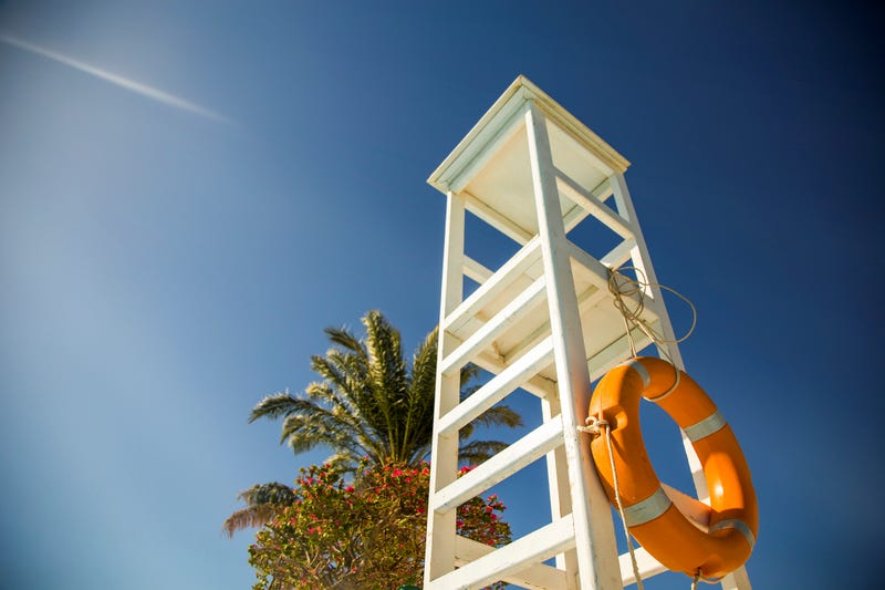 A white observation lifeguard tower near the palms with sun rays and beautiful sky