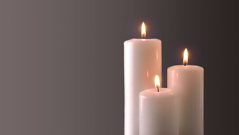 Three lit candles of staggered heights, set against a plain background