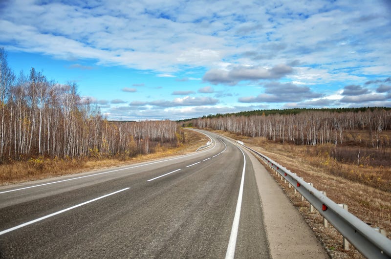 empty highway and beautiful birch trees with yellow leaves against a blue sky with clouds