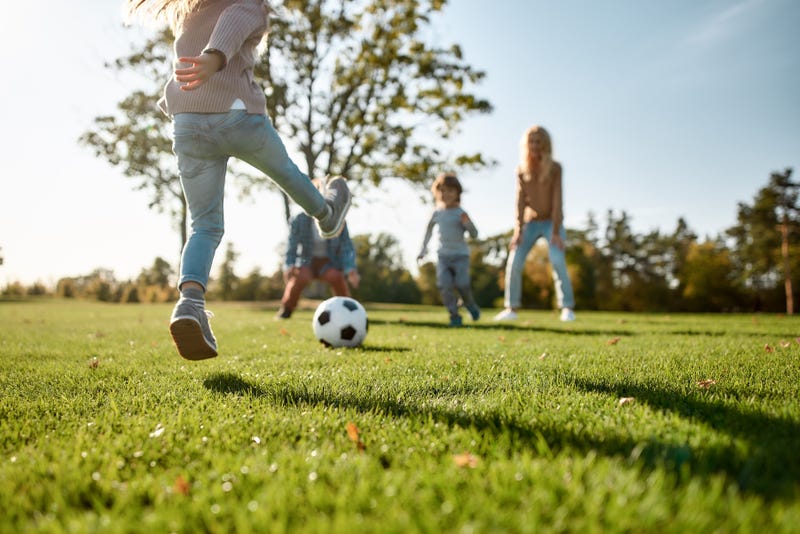 Cropped portrait of cheerful little girl playing football with her family in the park on a sunny day.