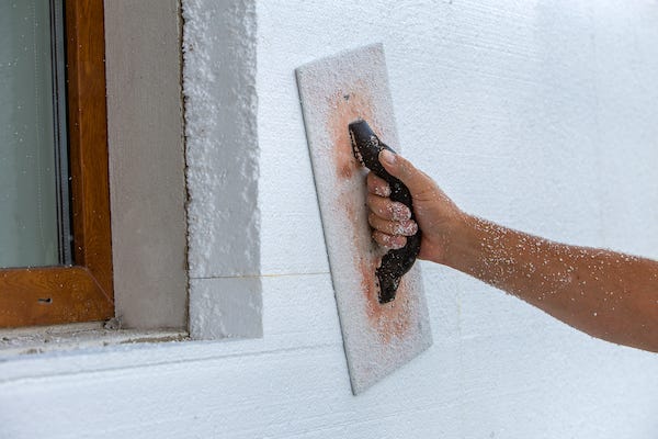 Hand of a worker with a tool for sanding and making smooth and even the surface of a house wall insulated with styrofoam insulation sheets