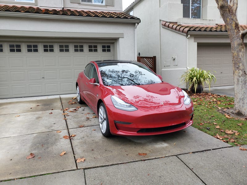 Red Tesla Model 3 automobile parked in the driveway of a suburban home.