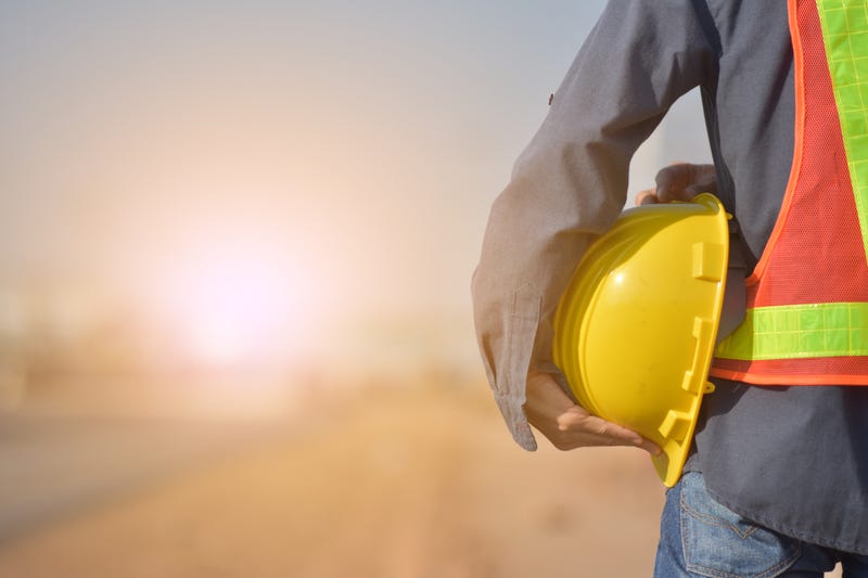 Engineer holding yellow hard hat with road construction background