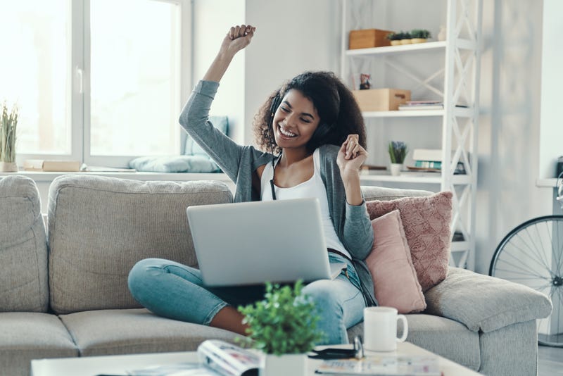 Happy young woman in casual clothing enjoying music and smiling while resting at home