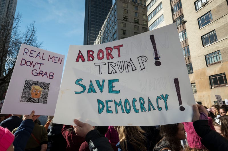 Marchers hold signs that say, "Abort Trump Save Democracy" and "Real Men Dont Grab" walking during the second annual Women's March in the borough of Manhattan in New York City, U.S. on Saturday, January 20, 2018.
