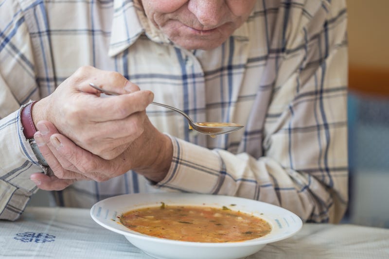 An elderly man with Parkinson's disease holds a soup spoon in both hands.