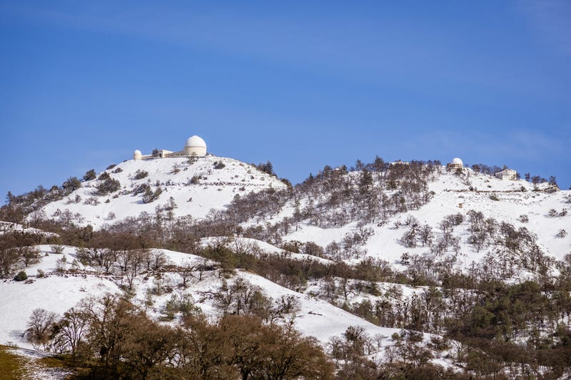View towards the top of Mt Hamilton on a clear winter day, snow covering the summit and the surrounding hills; San Jose, San Francisco bay area, California.