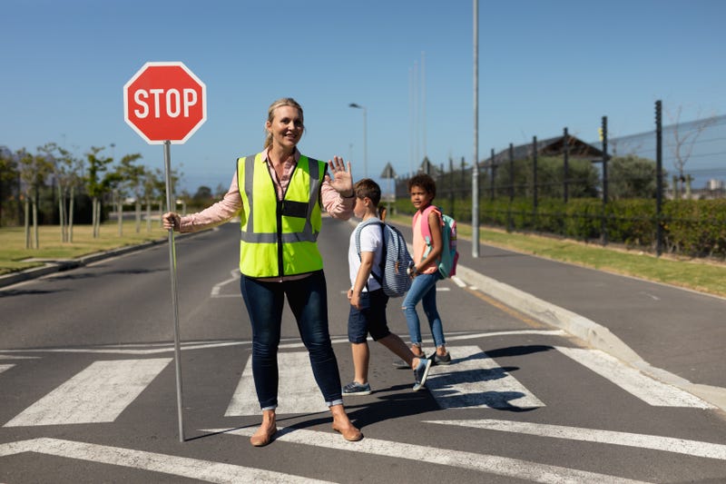 A school crossing guard leads children across a street