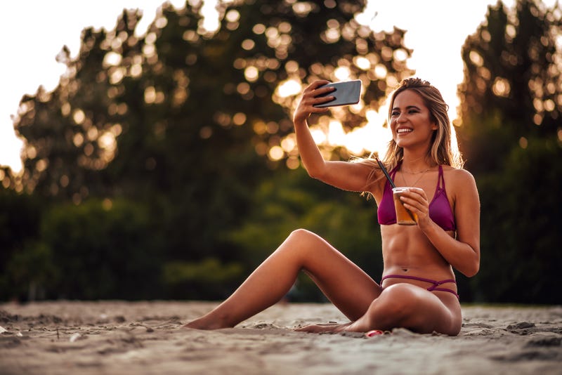 Girl sitting on a sandy beach with drink and smart phone, in the evening.