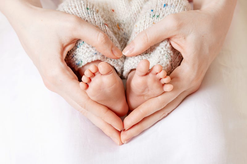 Baby feet in mother hands. Tiny Newborn Baby's feet on female Heart Shaped hands closeup. Mom and her Child. 