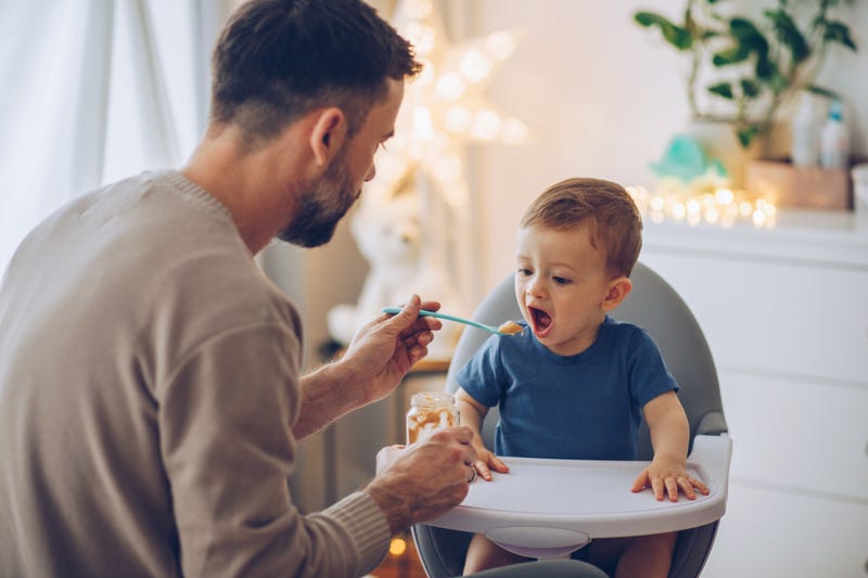 father feeding his little baby some baby food. baby's in a high chair