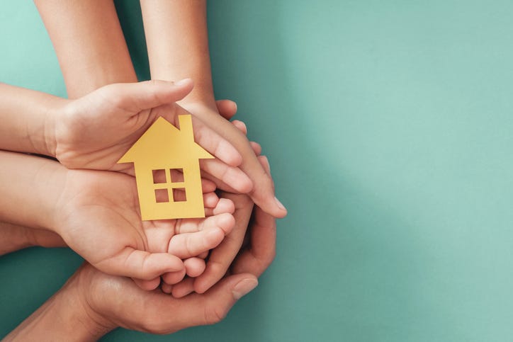 Hands holding yellow paper house on blue background,