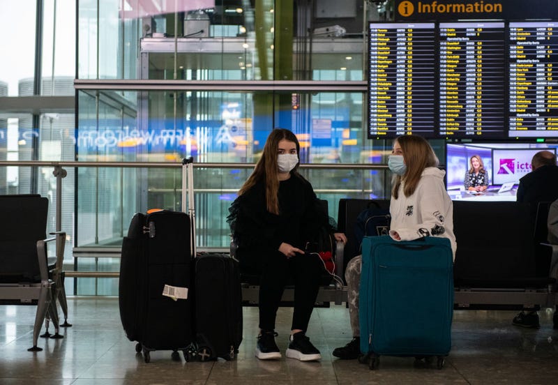 Airline passengers wearing face masks sit with their bags at departures at Heathrow Terminal 5 as the outbreak of coronavirus intensifies on March 15, 2020 in London, England.