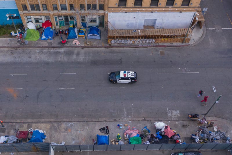 A police car passes homeless people on Skid Row after the new restrictions went into effect as the coronavirus pandemic spreads on March 20, 2020 in Los Angeles, California. 