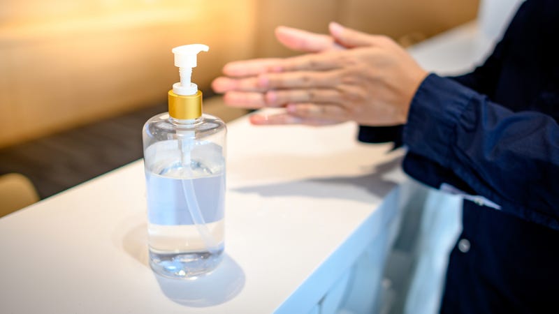 A person rubs their hands beside a hand sanitizer dispenser