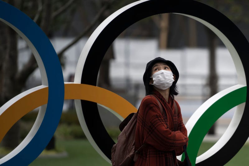 A woman wearing a face mask walks past the Olympic rings in front of the new National Stadium, the main stadium for the upcoming Tokyo 2020 Olympic and Paralympic Games