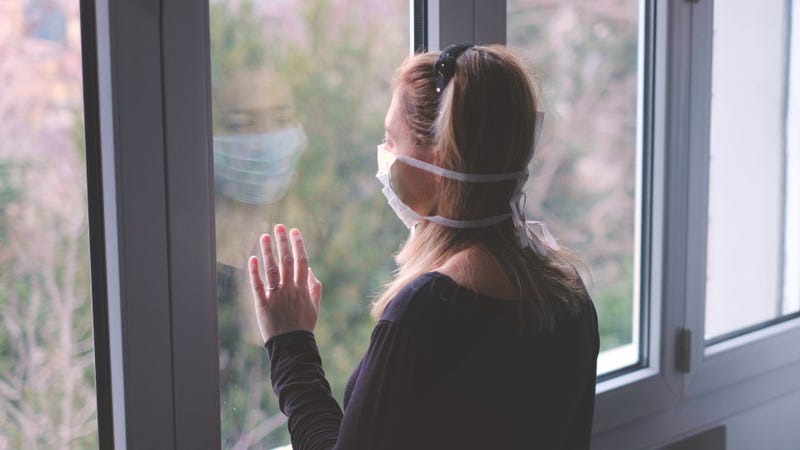 A woman in a medical mask looks longingly out a window