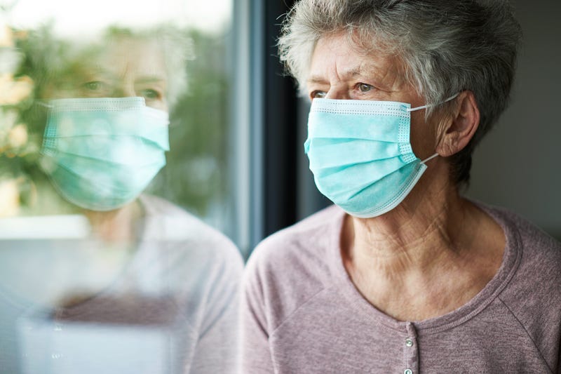 File photo of a woman wearing a surgical mask while looking out the window as she is in quarantine with COVID-19.
