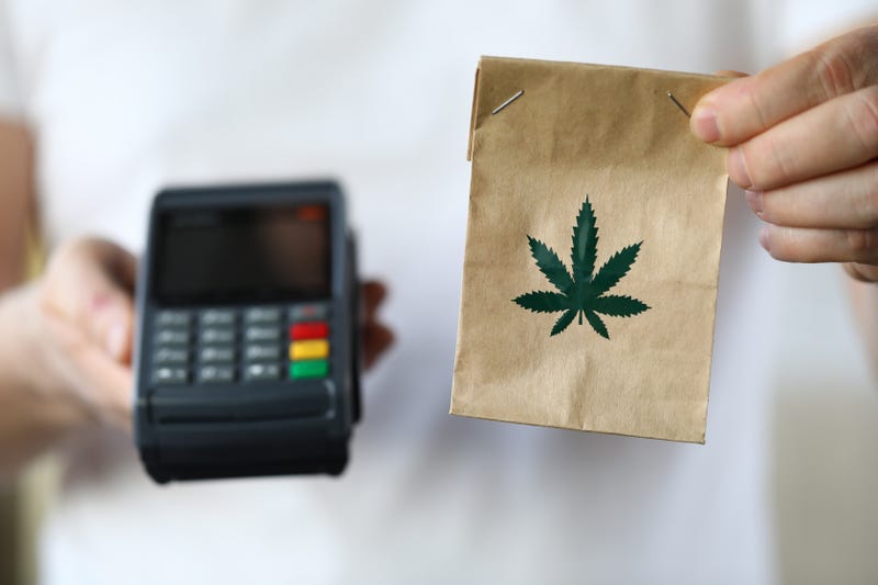 person holding a card reader and a brown paper bag with a weed leaf on it