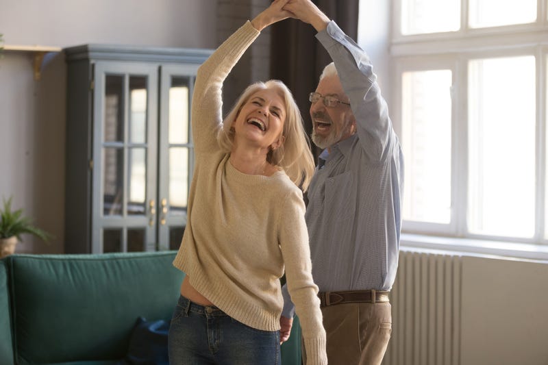 Overjoyed mature grey-haired Caucasian husband and wife have fun enjoy time together at home, happy elderly couple spouses dancing in living room, senior man lead sway smiling