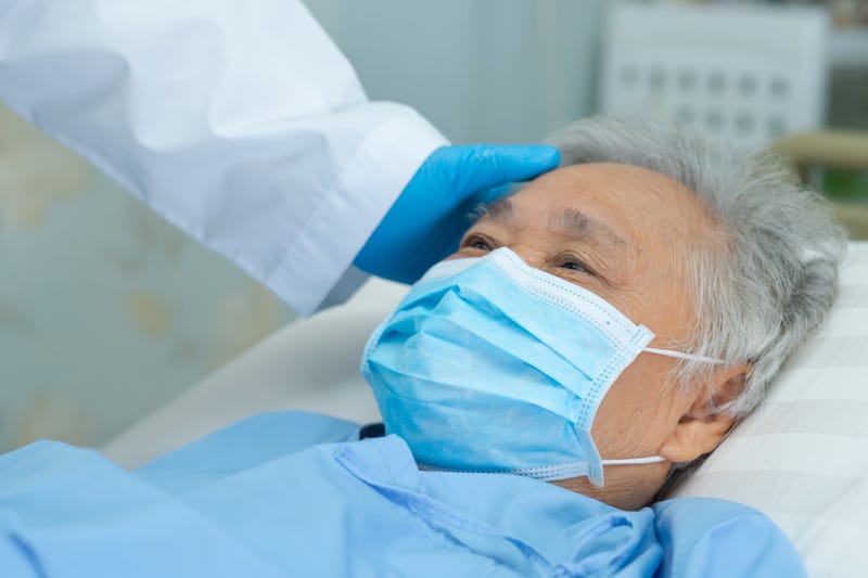 Doctor touching and checking senior patient wearing a face mask.