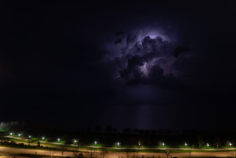 An intense thunderstorm cloud with blue or purple colors and lit up with numerous lightning strikes moves over Lake Michigan as cars pass by on Lake Shore Drive on Chicago's north side.