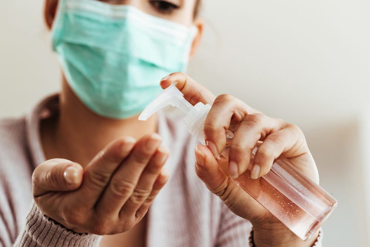 A woman using antibacterial hand gel while wearing a mask.