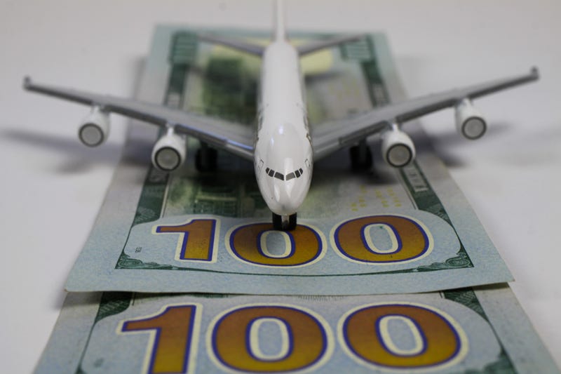 A toy airplane on top of hundred dollar bills, depicting expensive prices.