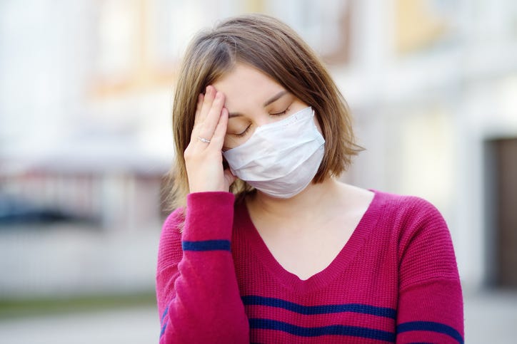 Young woman wearing a mask with a headache. 